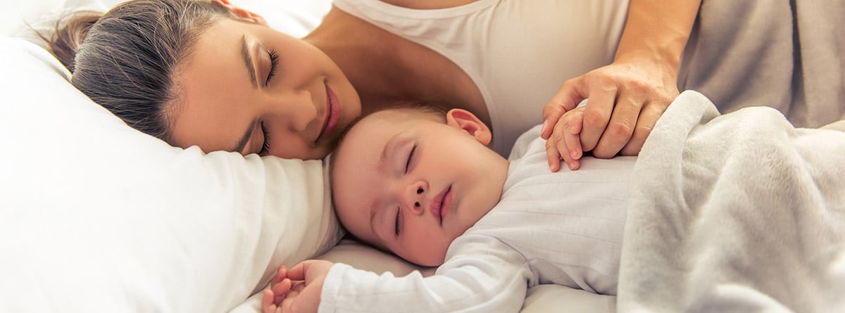 Vista lateral de una joven madre y su bebé durmiendo en la cama en casa