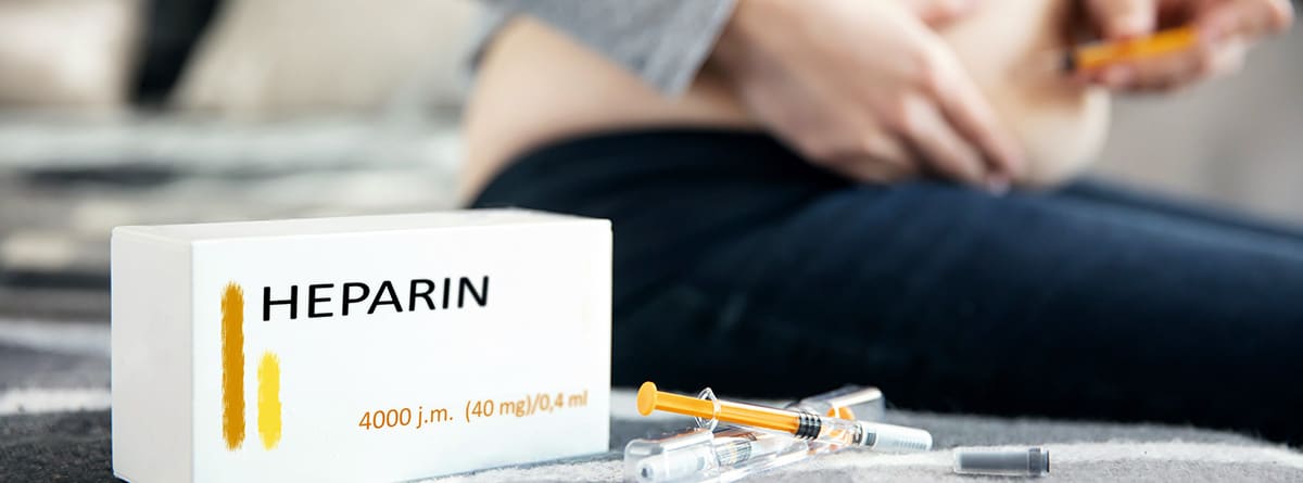 Caja de heparina con jeringuillas al lado y mujer inyectándose una dosis