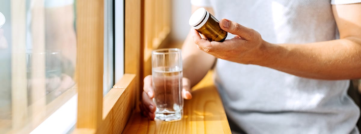 hombre con un frasco de medicamentos en una mano y en la otra un vaso de agua