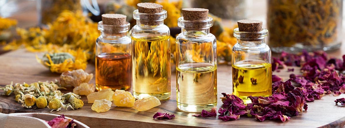 Aromaterapia: Botellas de aceite esencial con pétalos de rosa secos, manzanilla, caléndula y resina de incienso sobre una mesa de madera