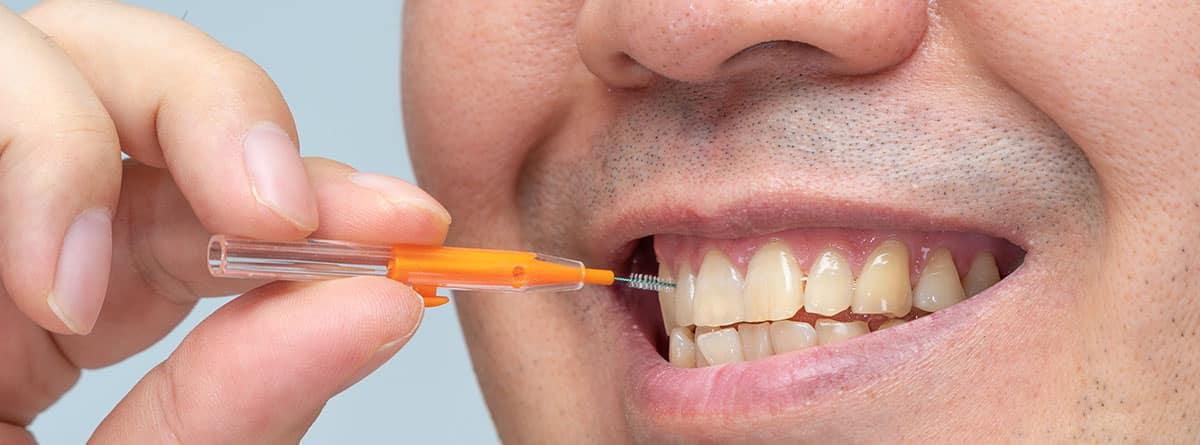 Hombre limpiándose los dientes con un cepillo interdental.