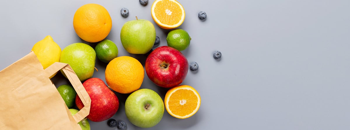 Bolsa de papel de compras llena de alimentos de frutas saludables sobre fondo gris