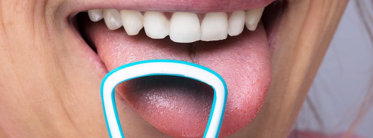 mujer con la boca abierta realizando una limpieza de la lengua con un aparato especial