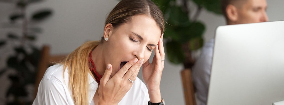 mujer bostezando con falta de sueño en oficina delante de un portátil