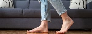 piernas femeninas caminan descalzas sobre un cálido suelo de madera cerca del sofá en la sala de estar de casa