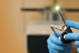manos de un profesional de la salud con guantes de nitrilo desechables que sostienen un anoscopio iluminado