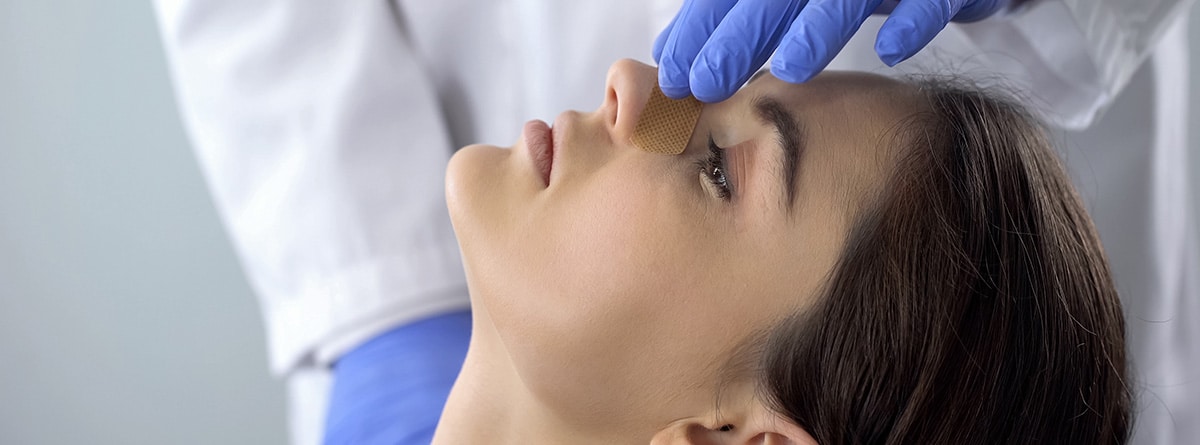 Manos de médico con guantes azules de látex poniendo una tirita sobre la nariz a una mujer