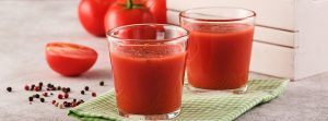 jugo de tomate en un vaso con tomates rojos maduros