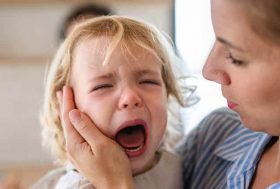 Niño de unos 2 años llorando en brazos de su madre, que trata de consolarle.