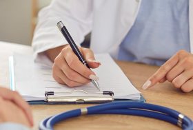 Manos de médico en consulta escribiendo informe médico