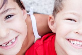 Dos hermanos pequeños con grandes sonrisas y dientes de leche faltantes