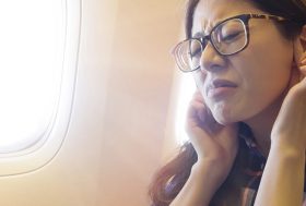 mujer joven con dolor de oídos viajando en avión