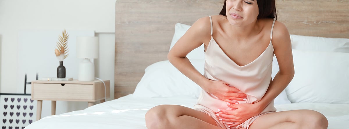 Mujer sentada en la cama con dolor en la barriga