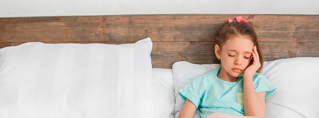 ¿Cómo saber si mi hijo padece migrañas? Niña sentada en la cama con una mano en la cabeza
