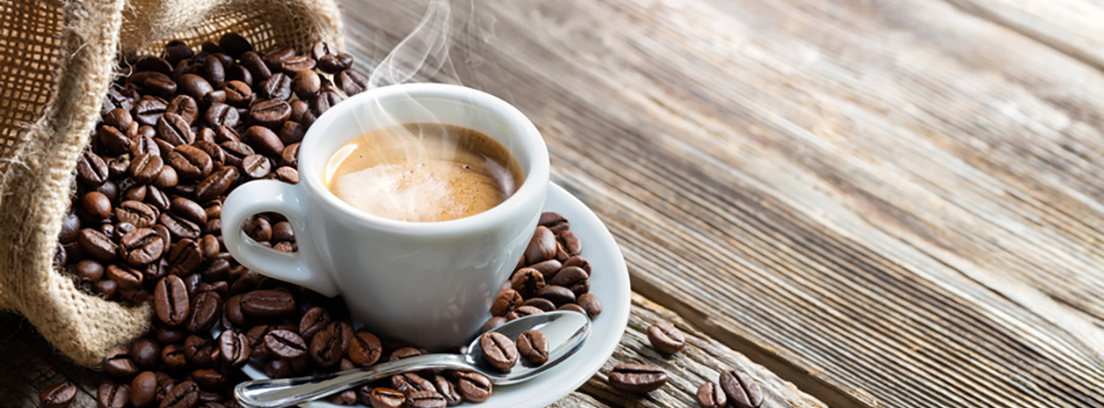 Taza blanca de café caliente con granos de café al lado