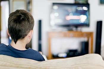 niño sentado en el sofá viendo la televisión relación entre obesidad infantil y publicidad en televisión