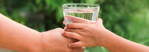 hidratación bebés y niños dos manos sujetando un vaso lleno de agua