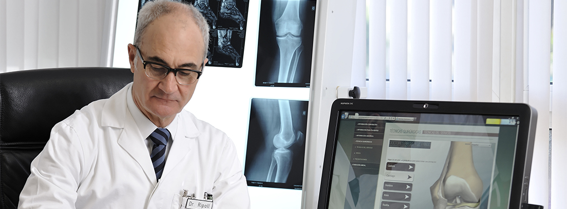 El Doctor Ripoll habla sobre las lesiones deportivas El Doctor Ripoll en su consulta escribiendo un informe en un folio y con el ordenador encendido con la imagen de una rotura de hueso