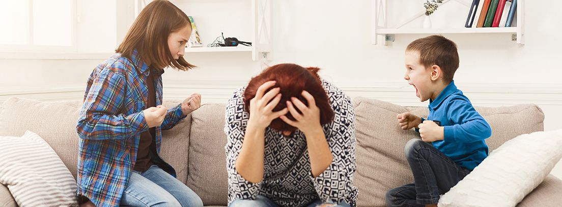 madre sentada en el sofá con las manos en la cabeza, una niña y un niño a cada lado gritando