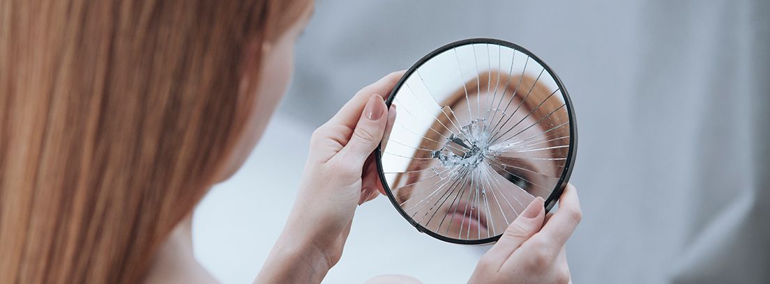 trastorno-dismórfico mujer con un espejo roto en las manos con su reflejo