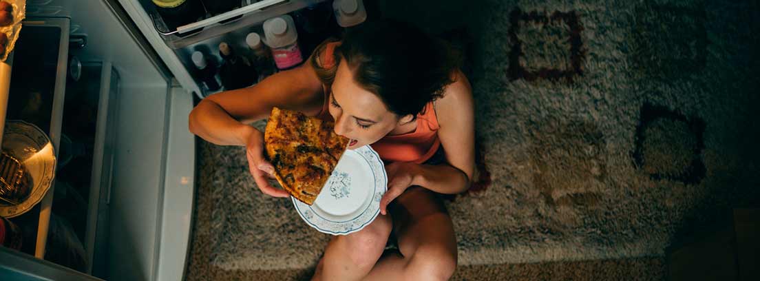 Atracones nocturnos mujer comiendo pizza por la noche con la nevera abierta
