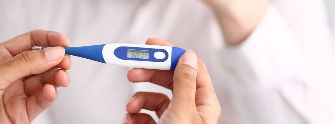 fiebre Qué temperatura se considera fiebre: manos cogiendo un termómetro