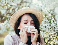 Alergia estacional: mujer con un sombrero de paja y un pañuelo en la naríz rodeada de plantas con polen