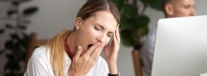 mujer bostezando con falta de sueño en oficina delante de un portátil