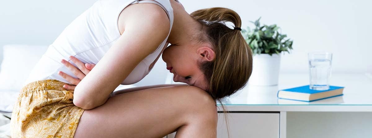 Mujer doblada tocándose la tripa, como si tuviera dolor