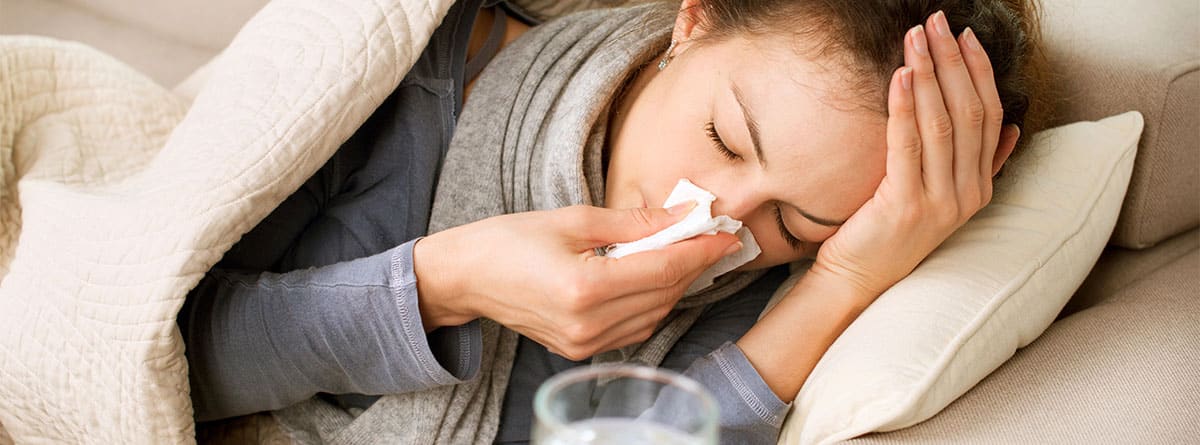 Mujer en la cama sonándose los mocos