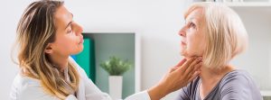 Mujer siendo revisada por una doctora, que le pone las manos en la garganta